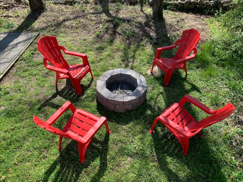 Fire pit surrounded by red Adirondack chairs on the lawn