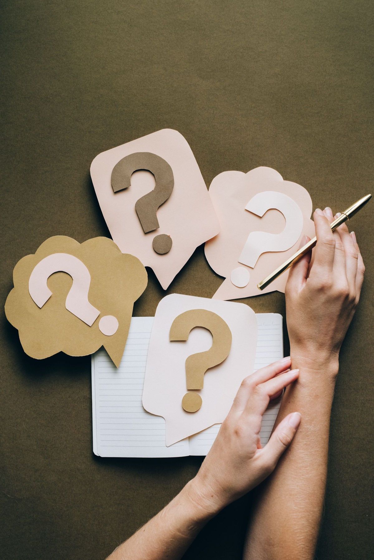 Hands arranging paper question marks over a notebook